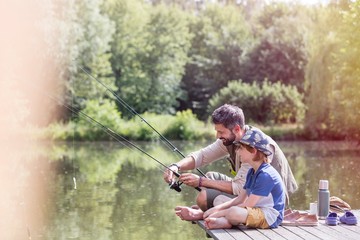 Full length of father assisting son fishing in lake while sitting on pier