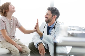 Doctor giving child patient high five in clinic