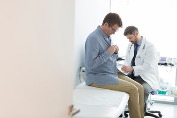 Obraz premium Doctor reading medical report while patient undressing for checkup at hospital