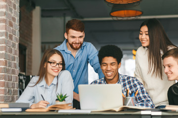 Obraz premium Happy classmates discussing project at library, using laptop