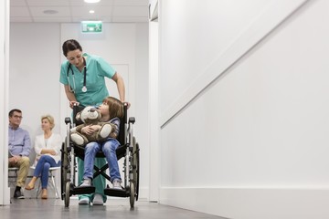 Nurse pushing child patient on wheel chair in clinic