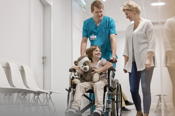 Nurse pushing child patient on wheel chair in clinic