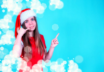 beautiful girl in Santa hat on blue background shows bell. invitation to the holiday.