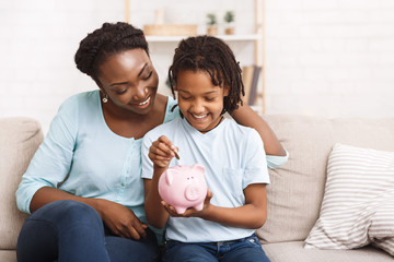 Little african american girl saving money to piggy bank