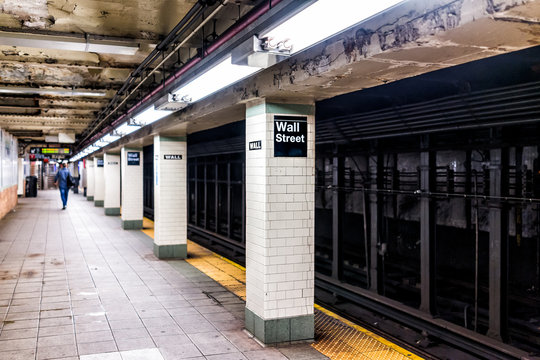 New York City, USA - October 30, 2017: Underground transit empty large platform in NYC Subway Station, railroad tracks, Wall street sign in downtown tiled column