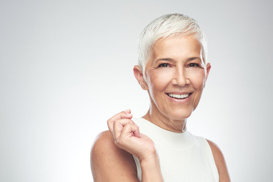 Beautiful smiling senior woman with short gray hair posing in front of gray background. Beauty photography.