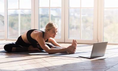 Keuken spatwand met foto Flexibel meisje dat thuis yoga doet en naar het scherm van de laptop kijkt © Prostock-studio
