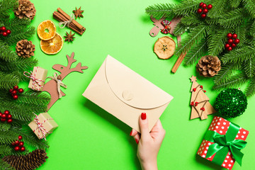 Top view of woman holding an envelope on green background made of holiday decorations. Christmas time concept