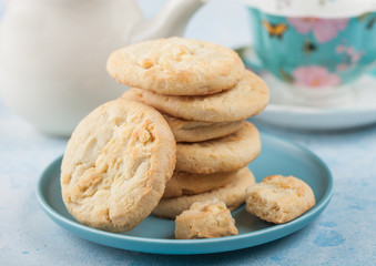 White chocolate biscuit cookies on blue ceramic plate with tea pot and cup on blue kitchen table background.