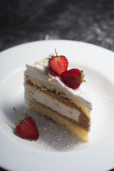 cake, a piece of delicate cake, with sliced fresh strawberries, on a white plate, on a white and gray abstract dark background. confectionery