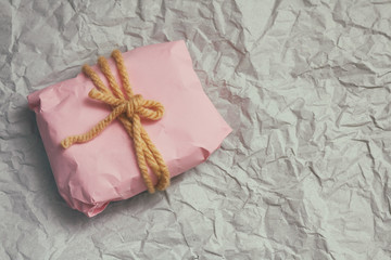 Gift box wrapped in light pink craft paper and tie yellow string. Christmas mood. Crumpled paper background. Present package. Delivery service. Soft craft pouch.