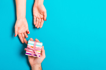 Top view of a man holding and giving a gift to a woman on colorful background. Receiving a present. Close up of holiday concept