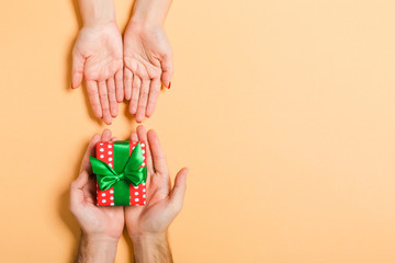 Top view of a man holding and giving a gift to a woman on colorful background. Receiving a present. Close up of holiday concept