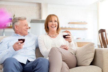 Fototapeta premium Smiling mature couple sitting on sofa while holding drinks at home