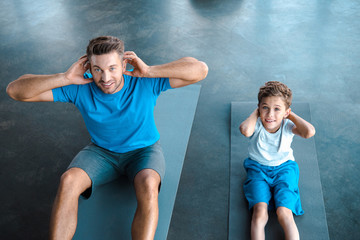 overhead view of cute kid and father exercising on fitness mats