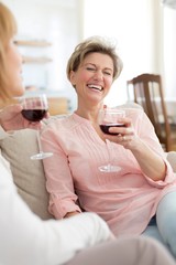 Cheerful mature friends with drinks sitting on sofa at home