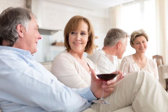 Smiling mature friends talking while sitting on sofa in living room at home