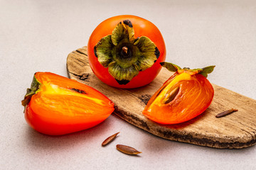 Ripe single persimmon. Fresh whole fruit, half sliced, seeds. Wooden cutting board, stone concrete...