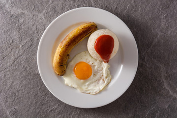 Arroz a la cubana.Typical Cuban rice with fried banana and fried egg on a plate on gray background. Top view	
