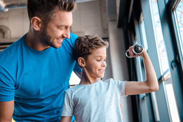 happy father looking at cheerful son exercising with dumbbell
