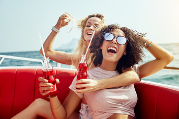 Laughing friends sitting on a boat having drinks during vacation