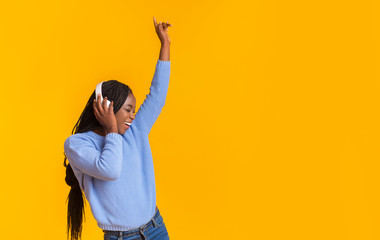 Funny afro girl enjoying music, dancing over yellow background