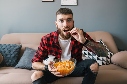 Photo of handsome focused man eating chips while watching sports match