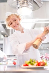 Smiling mature chef using peppermill on salad in plate at restaurant