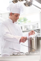 Confident mature chef cooking in steel pot on stove in kitchen at restaurant