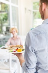 Waiter serving lunch to mature customer sitting at table in restaurant