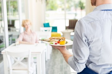 Midsection of waiter serving lunch to mature customer sitting at table in restaurant