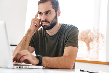 Fototapeta premium Image of handsome focused man typing on laptop while sitting