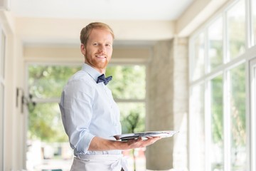 Fototapeta premium Portrait of confident young waiter holding tray while standing at restaurant