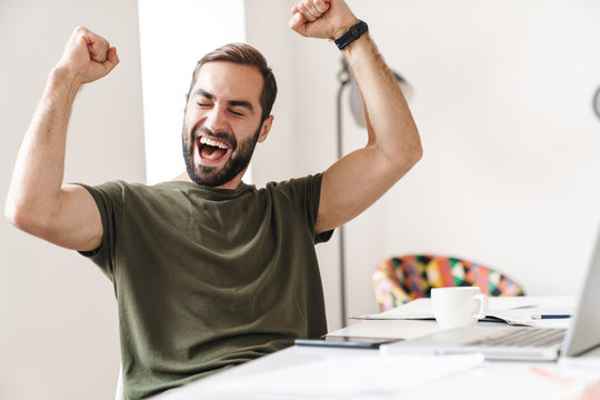 Image of delighted man sitting at desk and making winner gesture