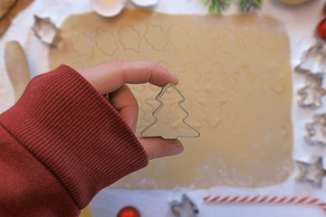 Top view of hand holding cookie cutter in shape of a Christmas tree in front of rolled out cookie...