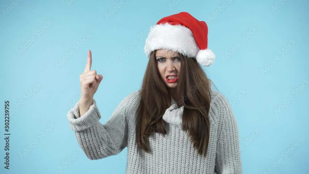 Wall mural Young woman in christmas santa hat say no by shaking wagging her finger, rejecting gesture, disagree sign. Serious angry face expression