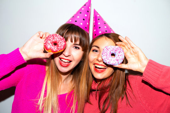 Portrait of two hungry young asian women holding two donuts isolated over  grey background.Picture of amazing two women friends eating donuts isolated over pink background. Looking camera
