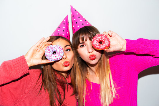 people, friends, teens and friendship concept - happy smiling pretty teenage girls with donuts making faces and having fun over blue background.Picture of amazing two women friends eating donuts 