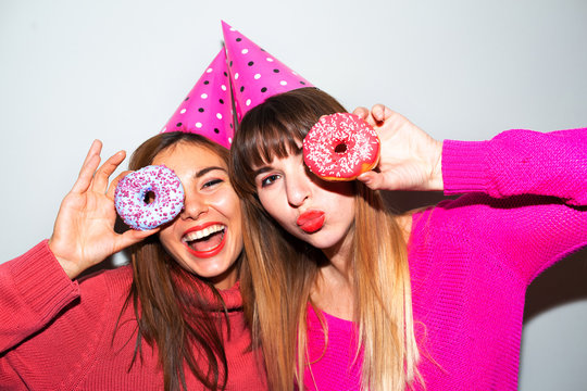 people, friends, teens and friendship concept - happy smiling pretty teenage girls with donuts making faces and having fun over blue background.Picture of amazing two women friends eating donuts 