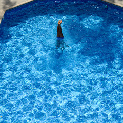 a man in the pool stands on his hands, sticking his legs out of the water top view