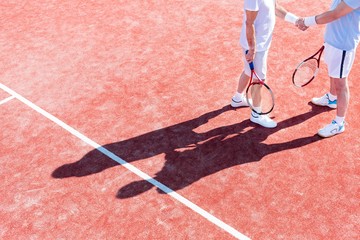 Low section of mature men shaking hands while standing on tennis court during match