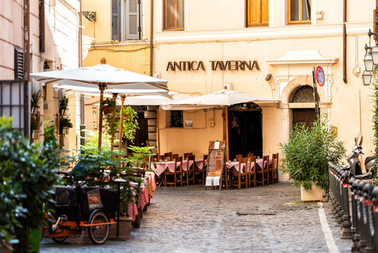 Rome, Italy - September 4, 2018: Italian restaurant tables, chairs, outside in traditional style, nobody on street cafe in historic city in morning, Antica Taverna sign