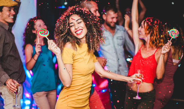 Young friends drinking champagne while dancing inside disco club - Happy people having fun eating candy lollipops at night party - Holidays and nightlife concept - Focus on woman face
