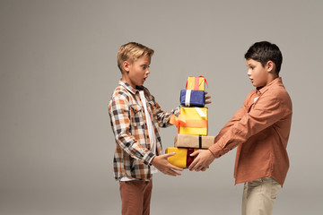 two amazed brothers holding stack of multicolored gift boxes isolated on grey