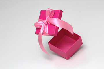 Pink gift box with satin ribbon. Open in motion. Space for goods and text. Unboxing process. Sale coupon template. White background.	