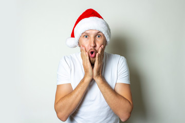 Young stupid man with a surprised face in a hat of Santa Claus on a white background. Christmas...