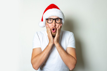 Young stupid man with a surprised face in a hat of Santa Claus on a white background. Christmas...