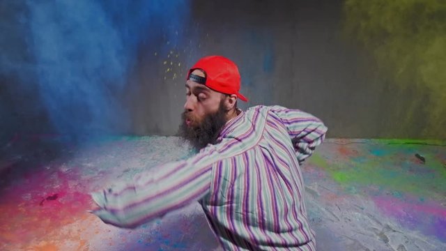 Man dancer showing break-dancing moves against colourful powder explosion