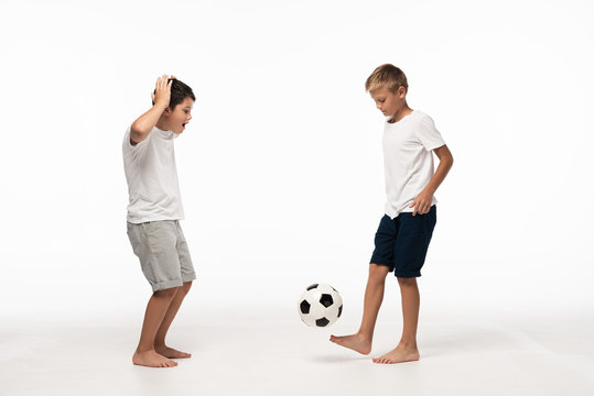 excited boy showing wow gesture while looking at brother playing with soccer ball on white background