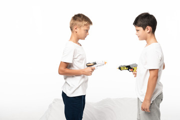 two brothers aiming at each other with toy guns while standing on bed isolated on white